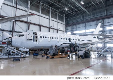 White passenger airplane under maintenance has opened weather radar and engine removed located nearby in the aircraft hangar 133549862