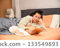 Grandma is lying on the bed playing with a tablet. 133549893