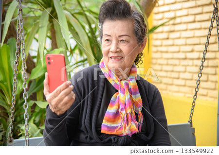 An elderly woman is sitting in a rocking chair in a park An elderly woman is sitting in a rocking chair in a park 133549922