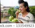An old woman is eating guavas. 133549923