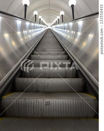 Low angle vertical photo of long metal escalator in grey metallic design. Along the escalator are lighting fixtures. Conceptual of upward mobility and the difficult career path 133550455