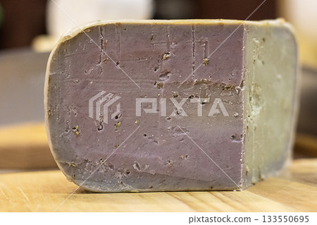 Purple cheese block on wooden board, rustic cheese tasting scene for gourmet cuisine Purple cheese block on wooden board, rustic cheese tasting scene for gourmet cuisine 133550695