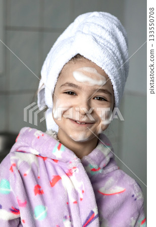 Happy young girl in purple bathrobe with towel on head and foam on face for bath time stock photo Happy young girl in purple bathrobe with towel on head and foam on face for bath time stock photo 133550708