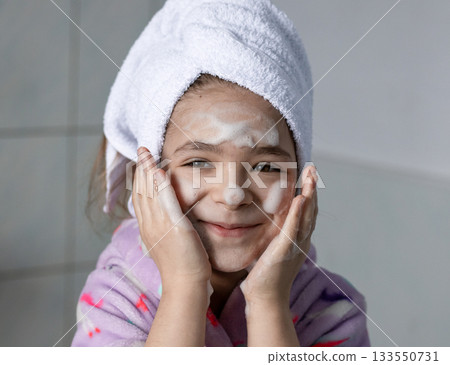 Smiling girl with soap on face and towel wrapped around head in bathroom 133550731