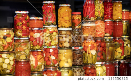 Colorful jars of pickled vegetables stacked at market stall showcasing homemade canning and variety 133550815