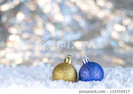 Two glittery Christmas ornaments sit in snow with twinkling lights in a festive winter scene Two glittery Christmas ornaments sit in snow with twinkling lights in a festive winter scene 133550817