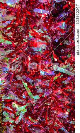 Abstract texture of bright red and iridescent metallic tinsel garland background with festive shine. Abstract texture of bright red and iridescent metallic tinsel garland background with festive shine. 133550847