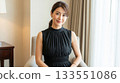 A Japanese woman in a black dress sitting in a hotel chair and smiling gently 133551086