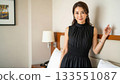 A Japanese woman in a black dress standing in a hotel room and staring at me 133551087