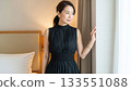 Elegant woman in a black dress standing by a hotel window looking out the window 133551088