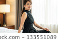 Elegant Japanese woman in a black dress sitting on a hotel bed and smiling 133551089