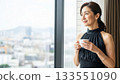 A Japanese woman in a black dress drinking coffee by the window in a hotel and smiling 133551090