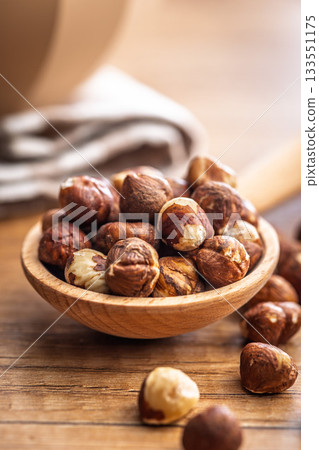 Peeled hazelnut kernels on spoon on wooden table. 133551175