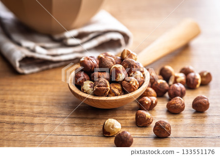 Peeled hazelnut kernels on spoon on wooden table. 133551176