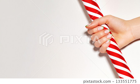 Beautiful woman palm with french manicure on nails holds red candy cane. Nails art design. Close-up of hands with trendy neon nails on striped print. Christmas in design for beauty and cosmetic Beautiful woman palm with french manicure on nails holds red candy cane. Nails art design. Close-up of hands with trendy neon nails on striped print. Christmas in design for beauty and cosmetic 133551775