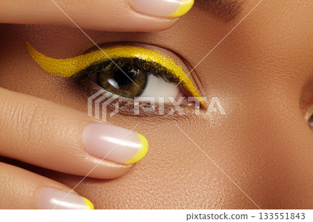 Close-up Female Eye with bright yellow Eyeliner Makeup. Neon Disco make-up and Fashion Manicure. Summer beauty style 133551843