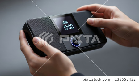 Radio alarm clock and speaker with digital display. Man holding a device for streaming music. 133552432