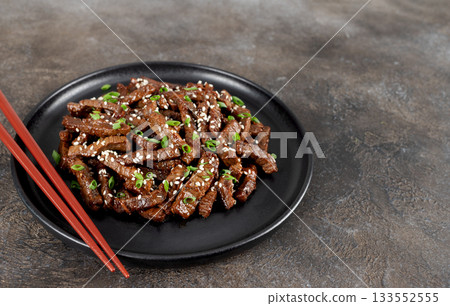 Fried teriyaki beef with sesame seeds and green onions on a brown background. Asian cuisine. Fried teriyaki beef with sesame seeds and green onions on a brown background. Asian cuisine. 133552555