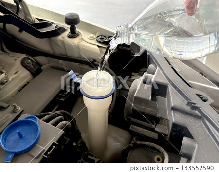 Filling the windshield washer reservoir under the hood of a car. Car maintenance. Filling the windshield washer reservoir under the hood of a car. Car maintenance. 133552590