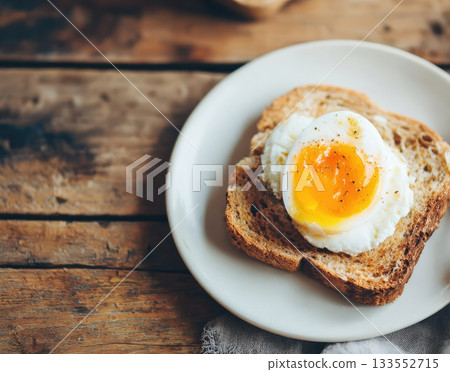 Poached egg golden yolk and whole wheat toast on white plate rustic wooden table background simple breakfast cozy morning healthy meal natural light inviting atmosphere 133552715