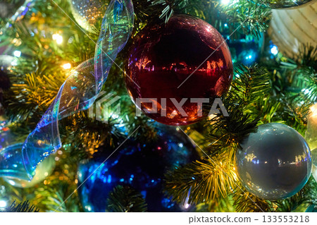 A glossy red ornament hangs with a flowing ribbon among shining lights. The close view shows rich reflections and festive bokeh. 133553218