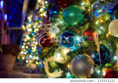 A decorated evergreen is covered with bright baubles, ribbons, and glowing lights. The colorful ornaments sparkle with rich bokeh in the night. A decorated evergreen is covered with bright baubles, ribbons, and glowing lights. The colorful ornaments sparkle with rich bokeh in the night. 133553222