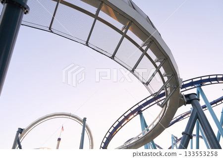 A sweeping coaster curve with safety netting arcs across the sky. Steel columns and bolts show crisp engineering details. 133553258