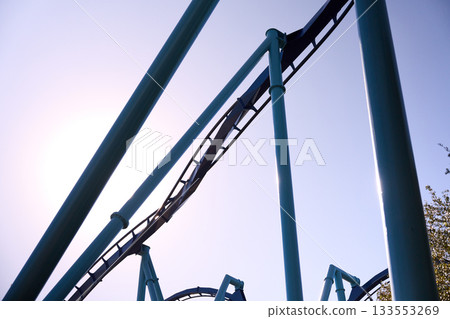 A steep track segment rises between tall columns in bright sunlight. The sleek structure highlights the energy of a modern thrill ride. A steep track segment rises between tall columns in bright sunlight. The sleek structure highlights the energy of a modern thrill ride. 133553269