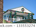 A bright tropical house is decorated with Christmas garlands and colorful ornaments. The festive decorations bring a holiday spirit to a sunny coastal setting. 133553274