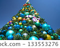 Low angle view of a tall Christmas tree covered with colorful baubles and tropical fish ornaments. The festive ocean-themed holiday decoration rises into a deep blue sky. 133553276