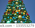 A tall Christmas tree is decorated with colorful baubles and starfish under a clear blue sky. Bright ocean-themed ornaments create a festive holiday display in a theme park. 133553279