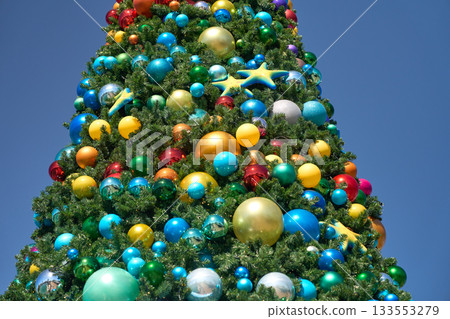 A tall Christmas tree is decorated with colorful baubles and starfish under a clear blue sky. Bright ocean-themed ornaments create a festive holiday display in a theme park. 133553279