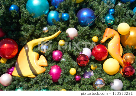 Christmas tree branches are filled with colorful baubles, a yellow tropical fish, and an orange seahorse. Bright holiday ornaments create a playful underwater holiday theme. Christmas tree branches are filled with colorful baubles, a yellow tropical fish, and an orange seahorse. Bright holiday ornaments create a playful underwater holiday theme. 133553281