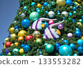 Large Christmas tree is covered with bright baubles and decorative tropical fish. Shiny holiday ornaments in many colors create a festive ocean-themed decoration. 133553282