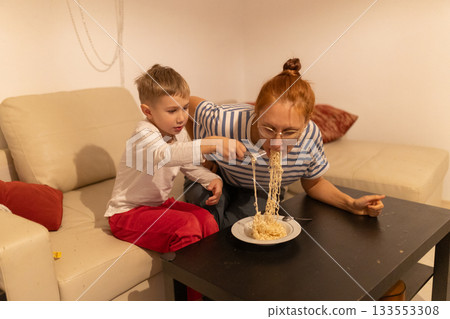 Boy feeding woman noodles at home Boy feeding woman noodles at home 133553308