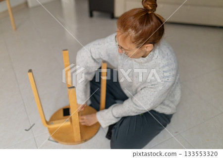 Woman assembling wooden stool with hex wrench at home 133553320