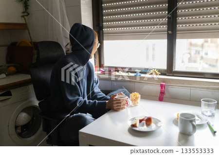 Person looking out window having breakfast at home Person looking out window having breakfast at home 133553333