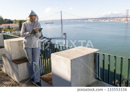 Woman using tablet overlooking tagus river and bridge 133553336