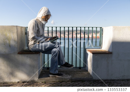 Person using digital tablet outdoors overlooking water 133553337