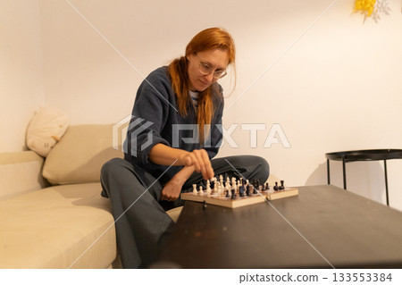 Woman playing strategic chess game at home 133553384