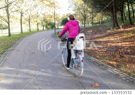 Woman riding bicycle on park path during autumn Woman riding bicycle on park path during autumn 133553532