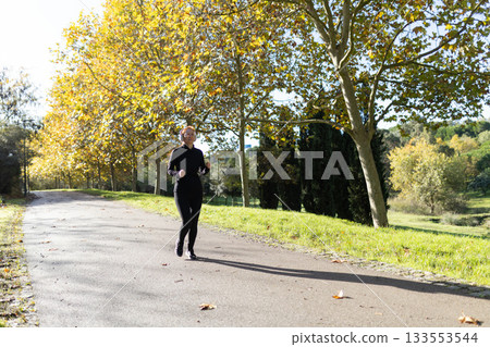 Woman running in autumn park path listening music Woman running in autumn park path listening music 133553544