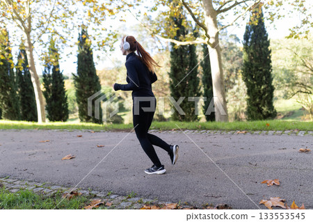 Young woman running with headphones in autumn park Young woman running with headphones in autumn park 133553545