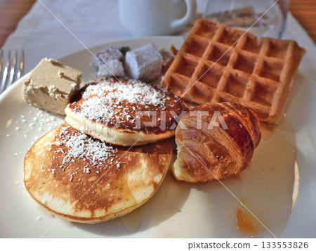 Delicious Breakfast Plate With Pancakes, Waffle, Croissant, And Pastry Trio On White Plate Delicious Breakfast Plate With Pancakes, Waffle, Croissant, And Pastry Trio On White Plate 133553826
