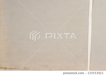 A beige fabric surface shows subtle woven texture with a vertical ribbon-like strip on the right side. Canvas texture, fabric surface close-up, natural simplicity A beige fabric surface shows subtle woven texture with a vertical ribbon-like strip on the right side. Canvas texture, fabric surface close-up, natural simplicity 133553921
