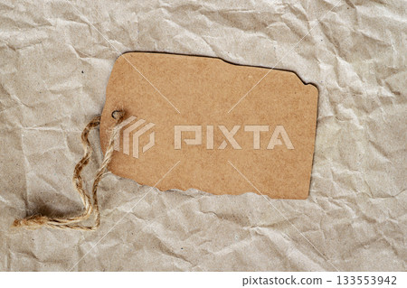 Brown kraft tag with rough twine lies on a textured paper background, natural surface. Simplicity of tag design, organic style, copy space 133553942