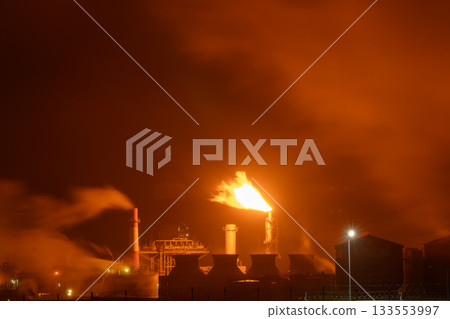 An industrial flare stack burns off excess gas with a large, bright orange flame and thick smoke An industrial flare stack burns off excess gas with a large, bright orange flame and thick smoke 133553997