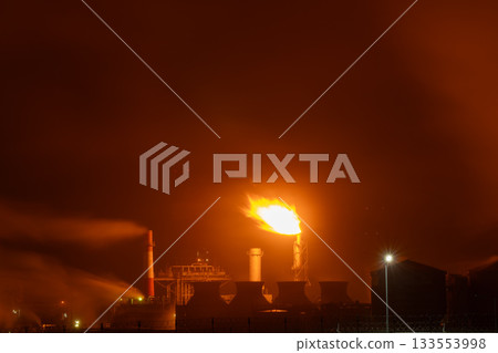 An industrial flare stack burns off excess gas with a large, bright orange flame and thick smoke An industrial flare stack burns off excess gas with a large, bright orange flame and thick smoke 133553998