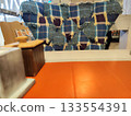 Wooden table with an orange surface and adjacent chair covered by a patchwork quilt, displaying a blue plaid pattern with frayed edges 133554391