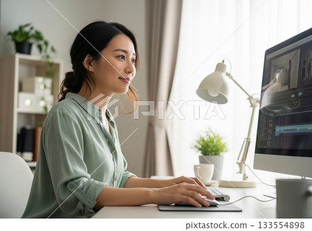 A woman working on a video editing task on a computer in a bright workspace at home 133554898